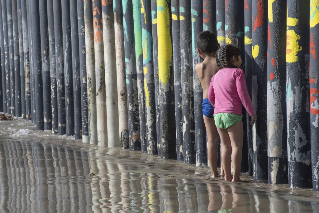 Two children look through a border wall on the beach in Tijuana.