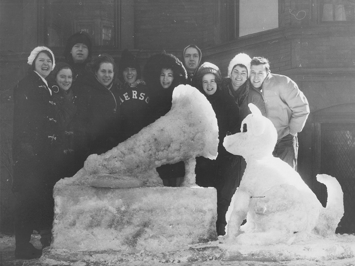 students stand behind snow sculpture of dog and gramophone, in black and white