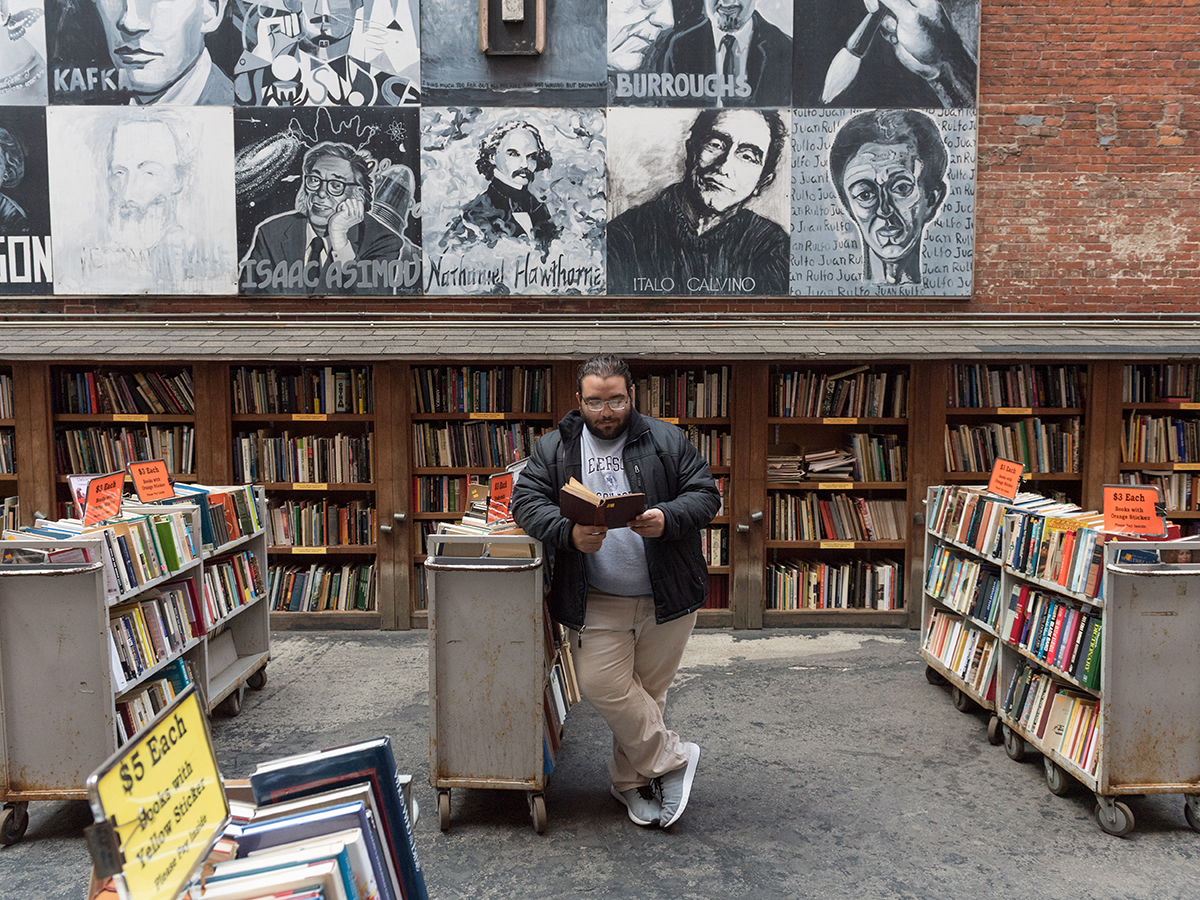 man leaning against bookshelf reading