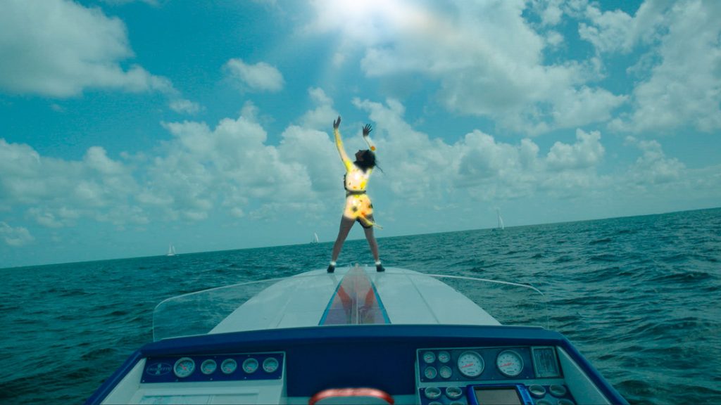 A woman stands on the front of a speedboat looking up to the sky.