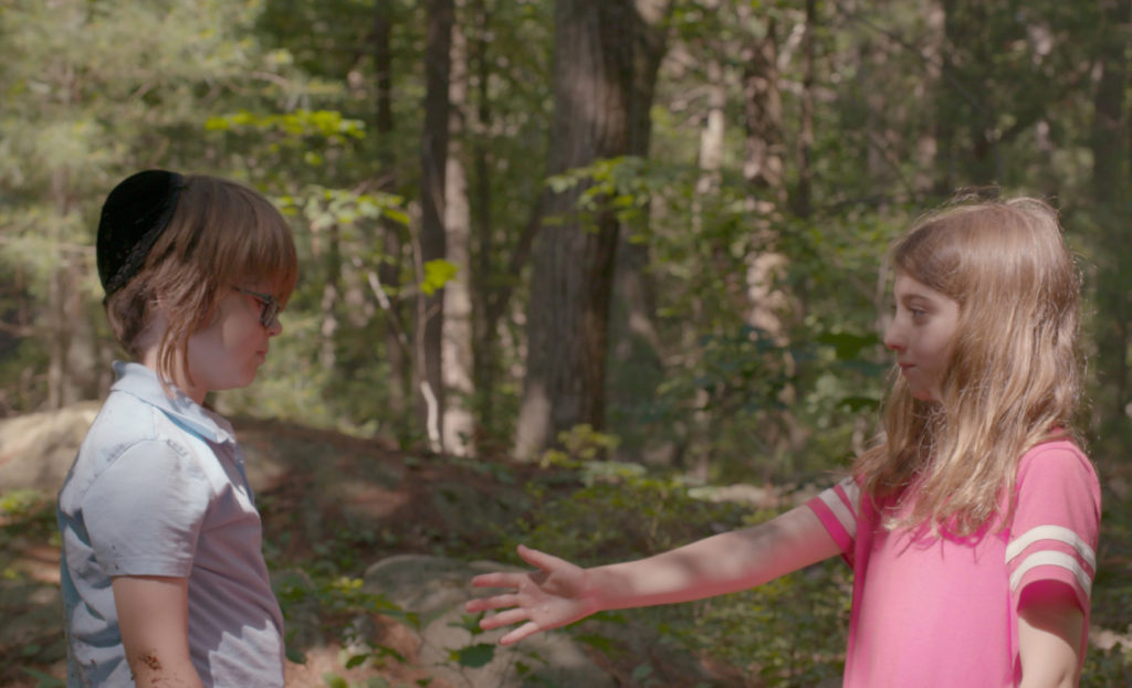 little girl extends hand to little boy in woods