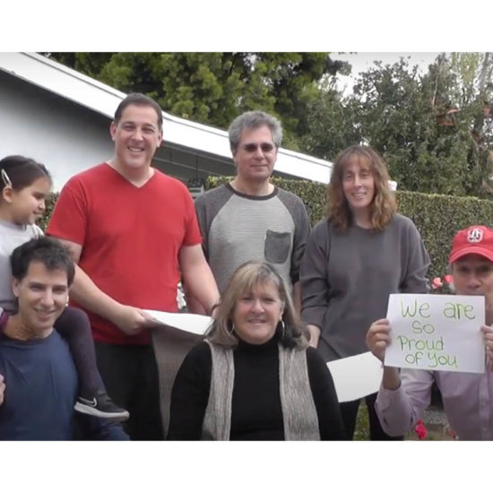 A family together holding a sign congratulating a family member on graduating from Emerson College.