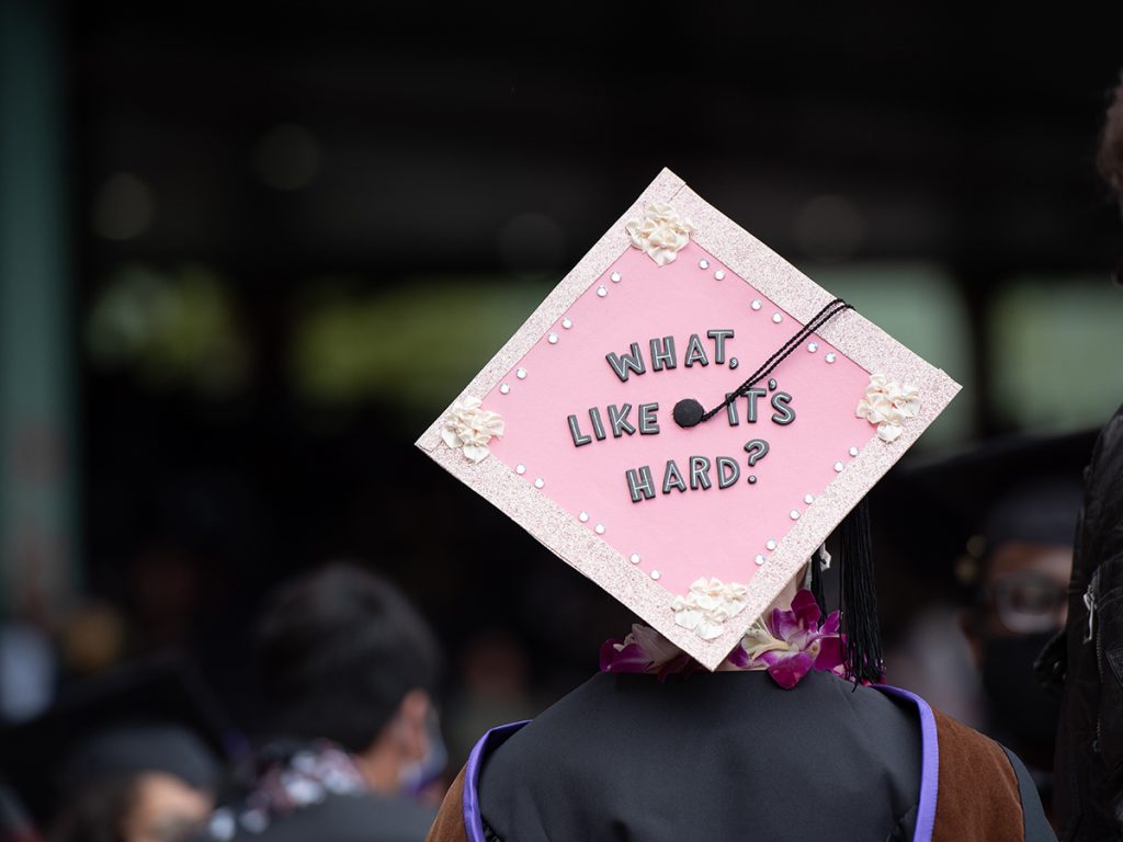 woman wearing mortarboard decorated in pink reading What Like It's Hard?