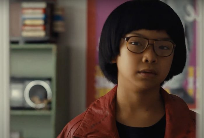 a young Asian boy in a red jacket and glasses looks in a mirror