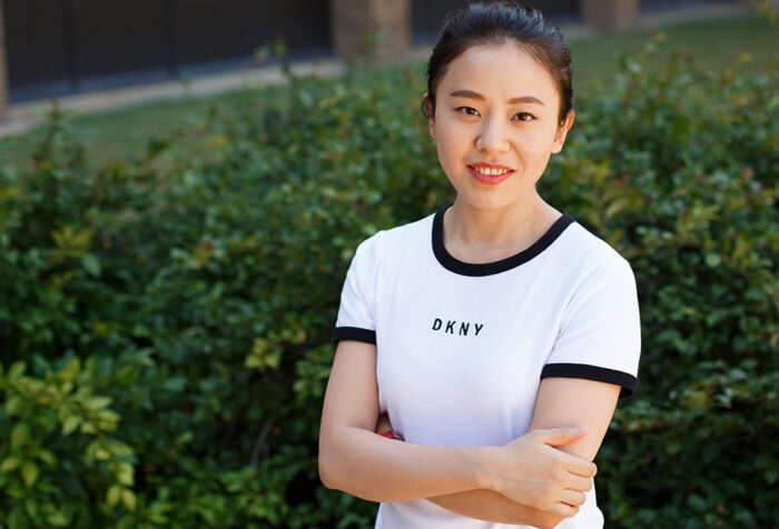 Zhao Peng in white tshirt, arms crossed, in front of hedges