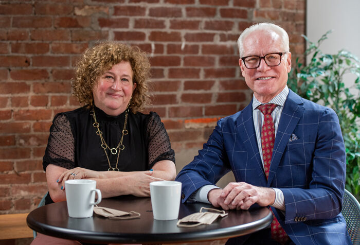 Sharon Topper and Tim Gunn seated at table in front of brick wall