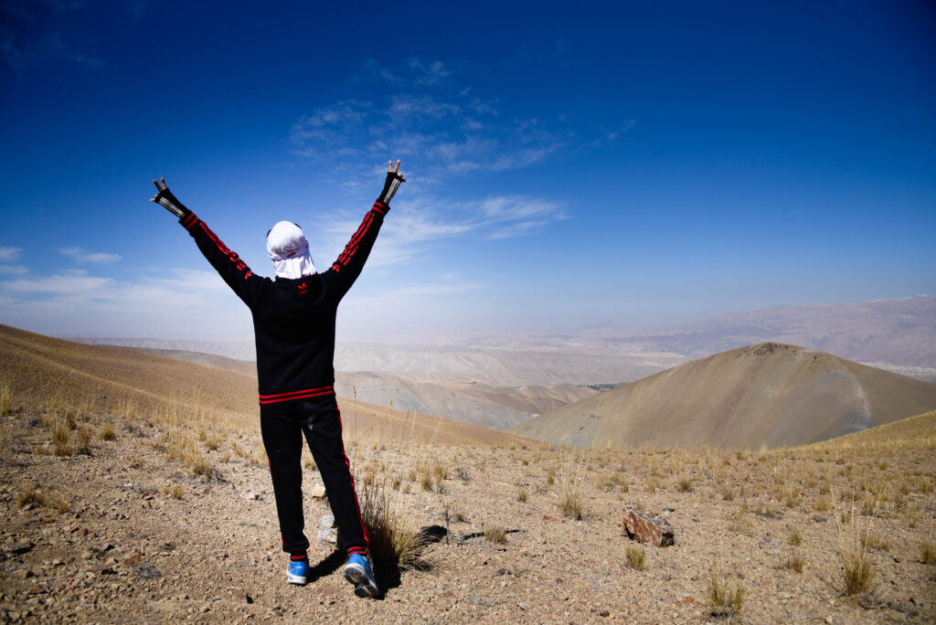 A person holds their hands up in the air while overlooking a hilled landscape
