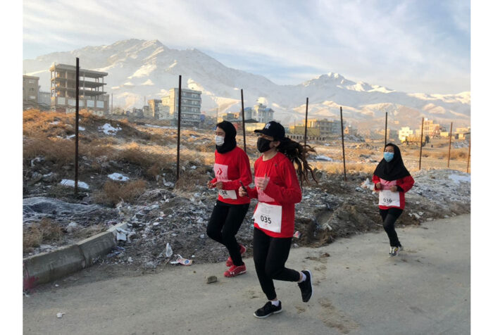 Three women run with snow capped mountains in the far background