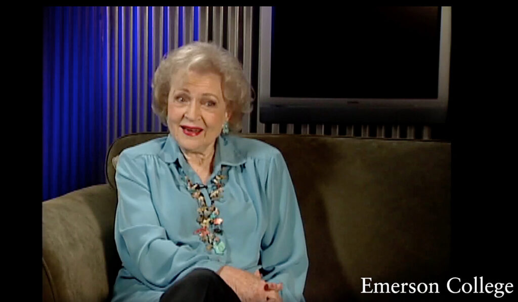 Betty White speaks on green couch with screen in background