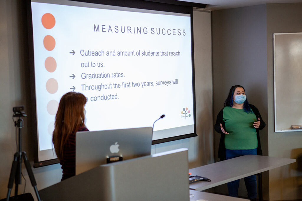 two women give presentation in front of screen captioned "measuring success"