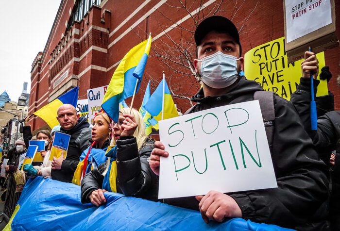 protestor holding sign reading "stop putin" others holding Ukrainian flag