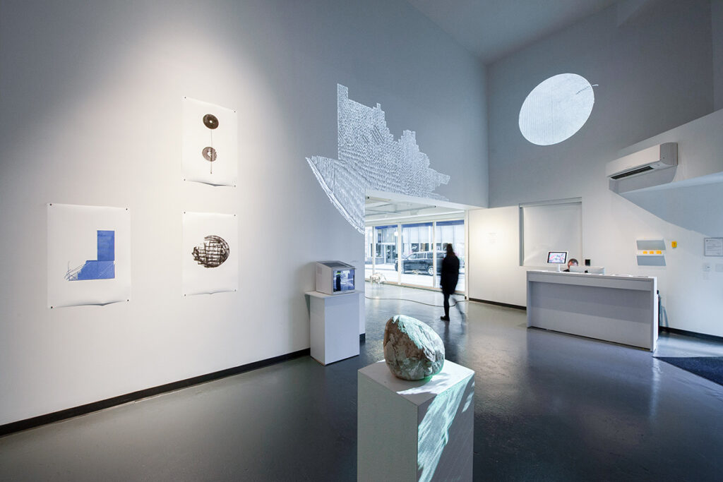 photo of Media Art Gallery, with projection art, ink drawings, reception desk, and man walking toward back of gallery