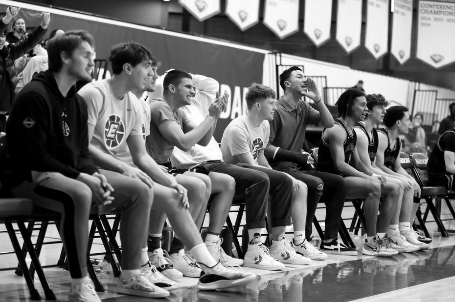 Basketball players sit on a bench together cheering on their teammates