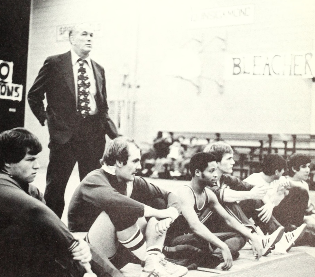 Wrestling coach stands behind players sitting on mat