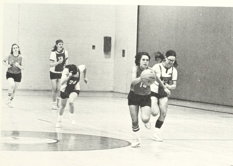Woman dribbling basketball ahead of other players