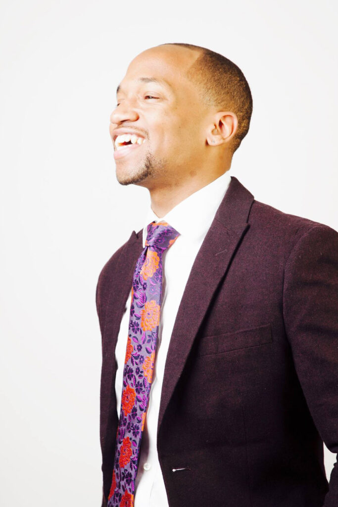 Deion Hawkins in burgundy suit and floral tie, laughing in profile