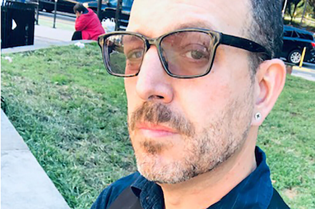 Jonathan Papernick seated outside in blue shirt, black vest
