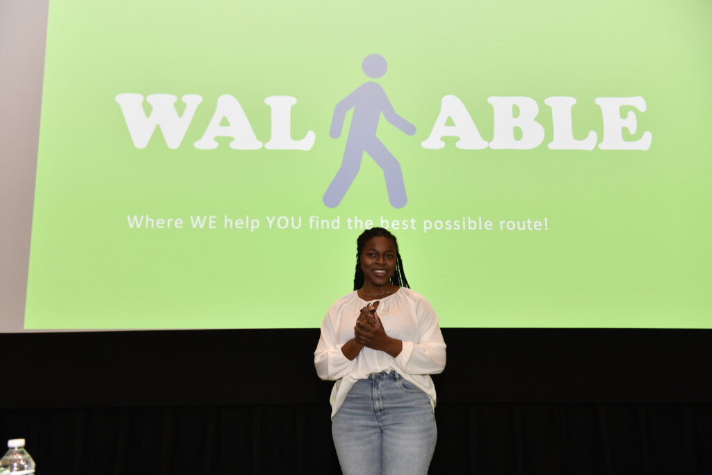 Woman stands in front of large screen that says WALKABLE