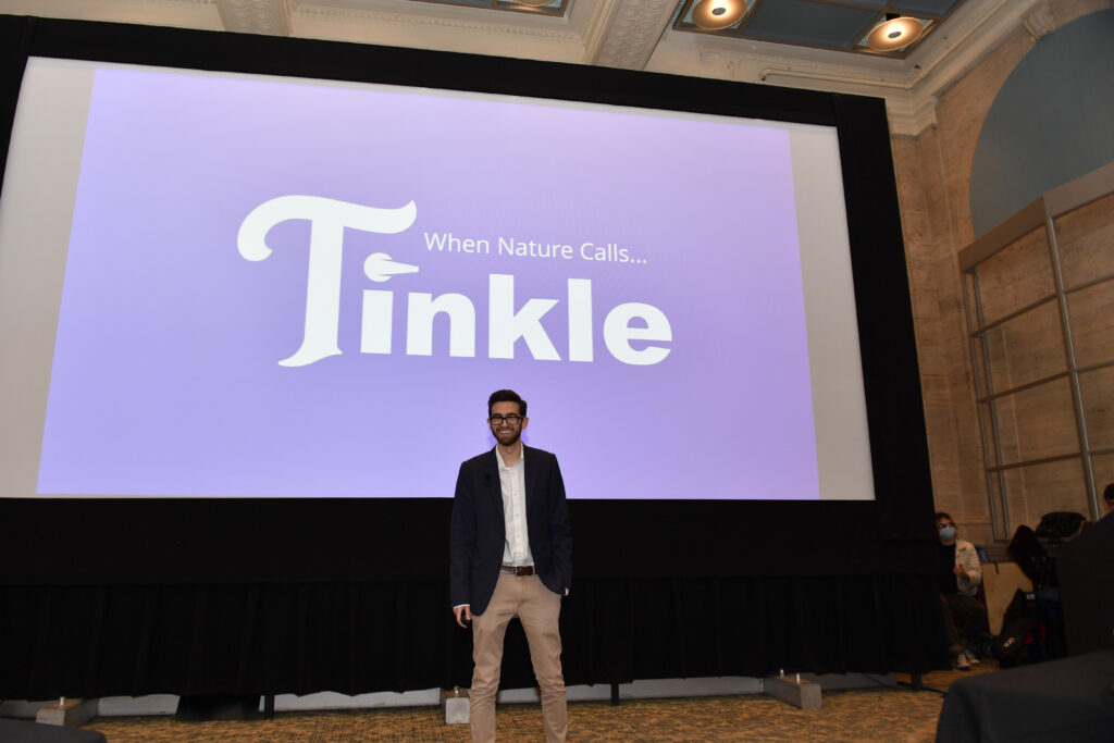 A man stands in front of a large screen that says Tinkle