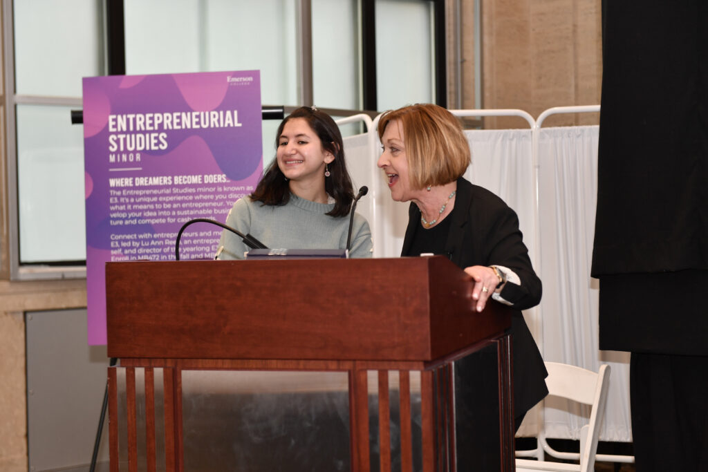 Two women smile and laugh while behind a lectern
