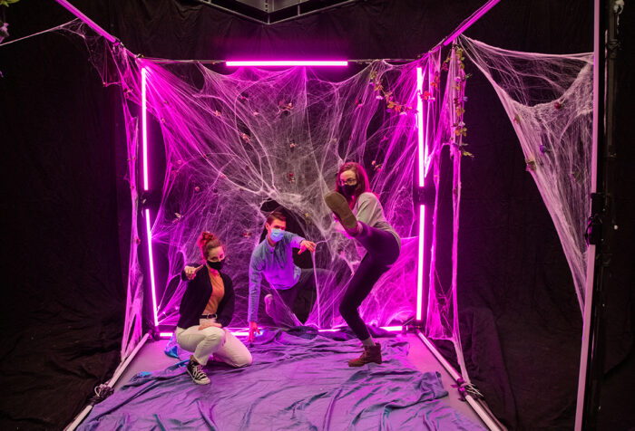 three women dance inside a cube made of pink neon light and fabric