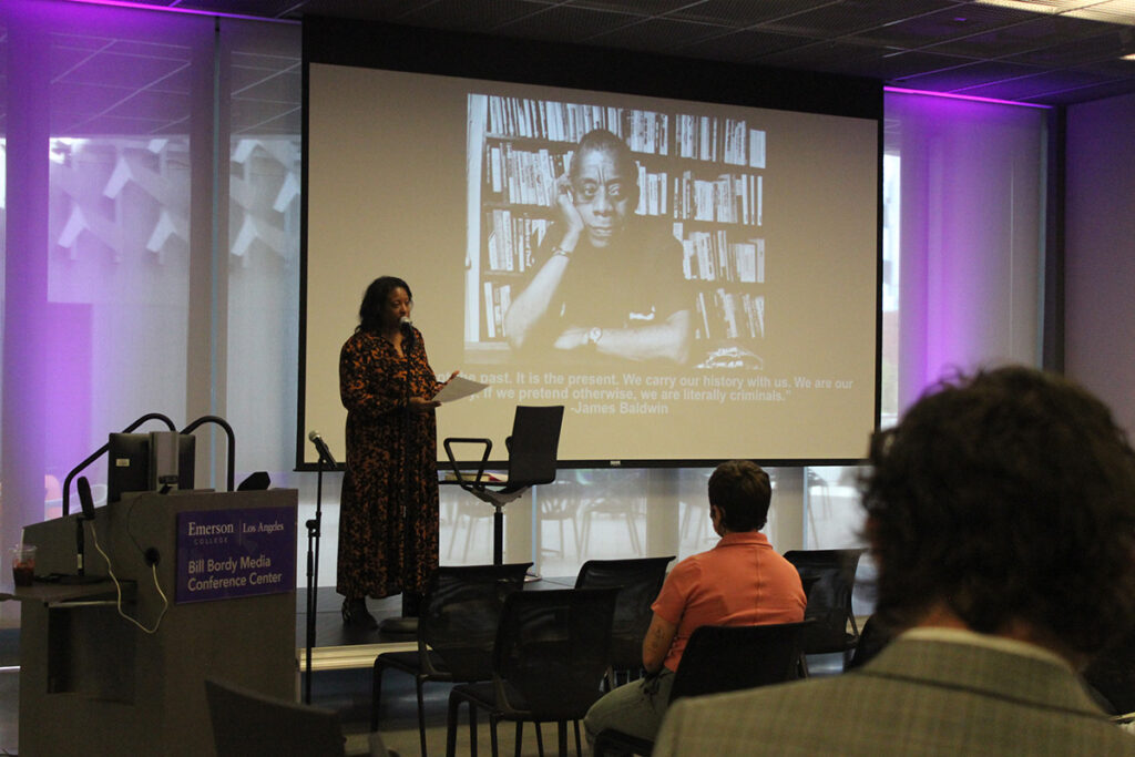 Shana Lloyd lectures in front of screen showing photo of James Baldwin, audience members in foreground