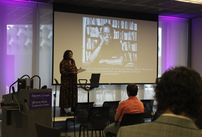 Shana Lloyd lectures in front of screen showing photo of James Baldwin, audience members in foreground
