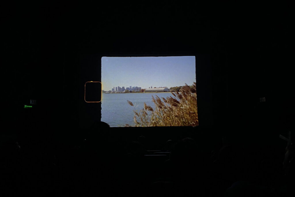 darkened theater with image of city skyline rising up behind water projected onto black screen