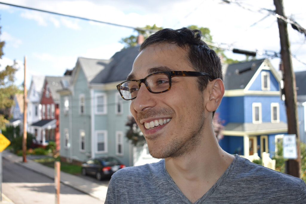 man in glasses and grey t-shirt with houses in the background