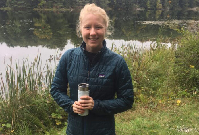 woman in fleece holding a water bottle in front of a pond