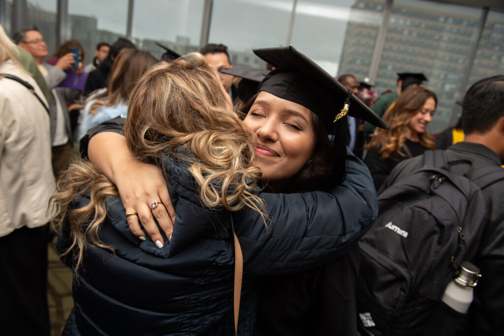 A graduate smiles with eyes closed as they embrace another person