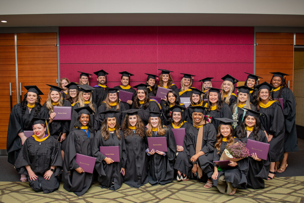 A group of graduates pose together in caps, gowns, holding diplomas