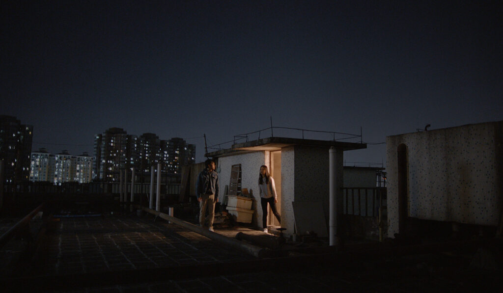 a man and woman talk on a rooftop at night