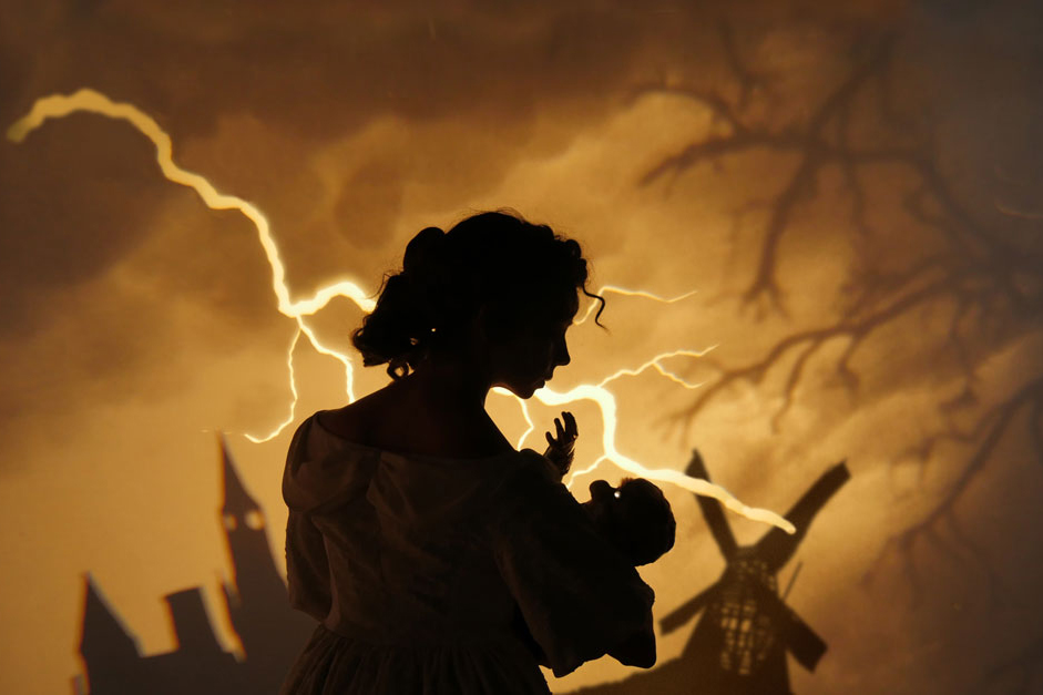 silhouette of woman, buildings, windmill, lightning bolt over sepia tone background