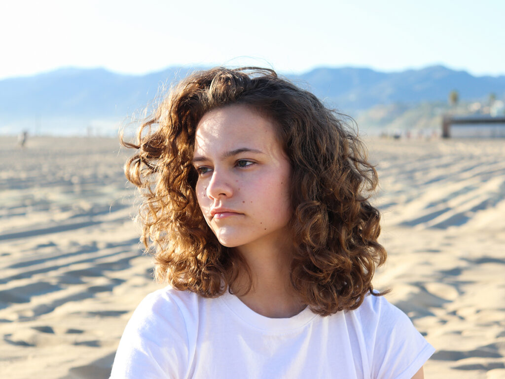 woman with brown curly hair in white t-shirt on sandy beach
