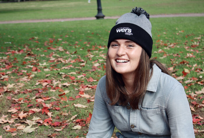 woman in WERS winter hat sits on grass covered with fallen leaves