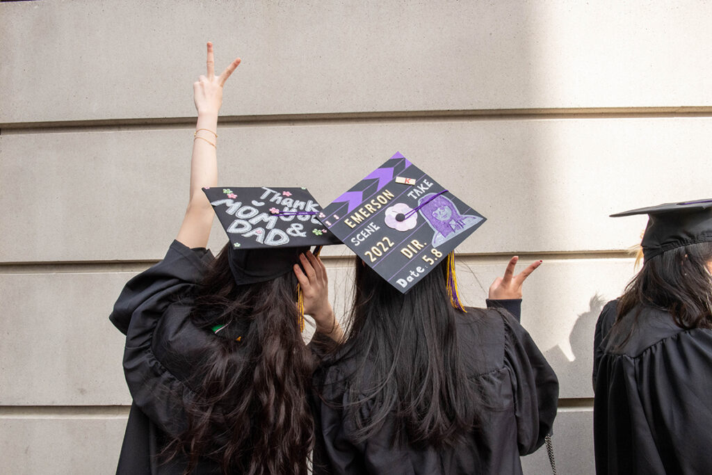 Two women with decorated mortarboards stand making peace sign with backs to camera