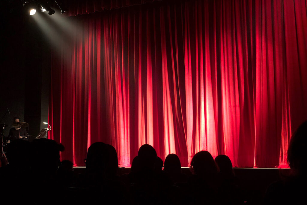 spotlight on red theater curtain with audience heads silhouetted in front