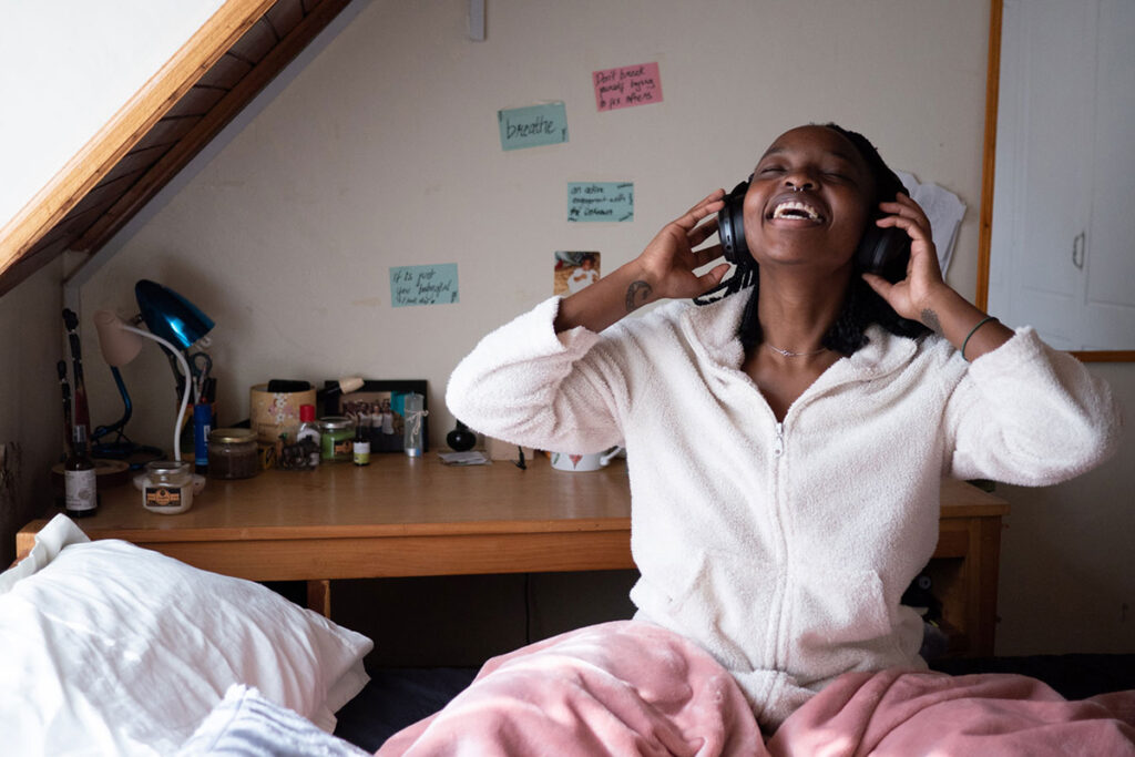 Young black woman wearing headphones closes eyes and smiles in bedroom