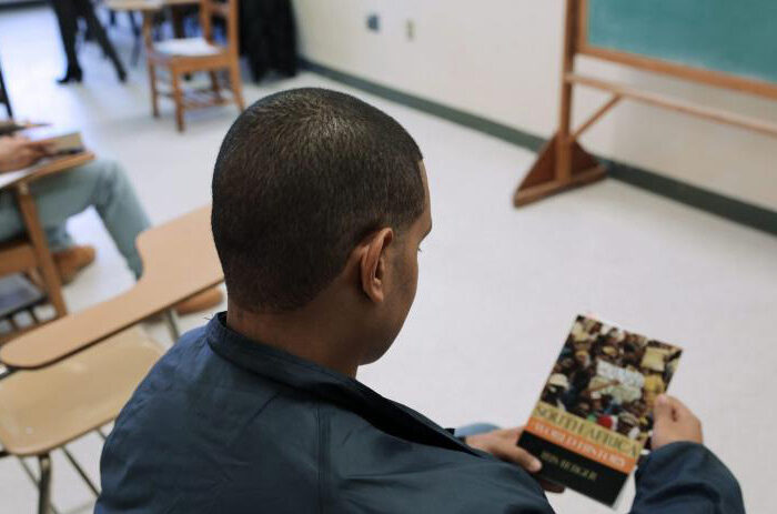 Over the shoulder of man looking a book while sitting in classroom