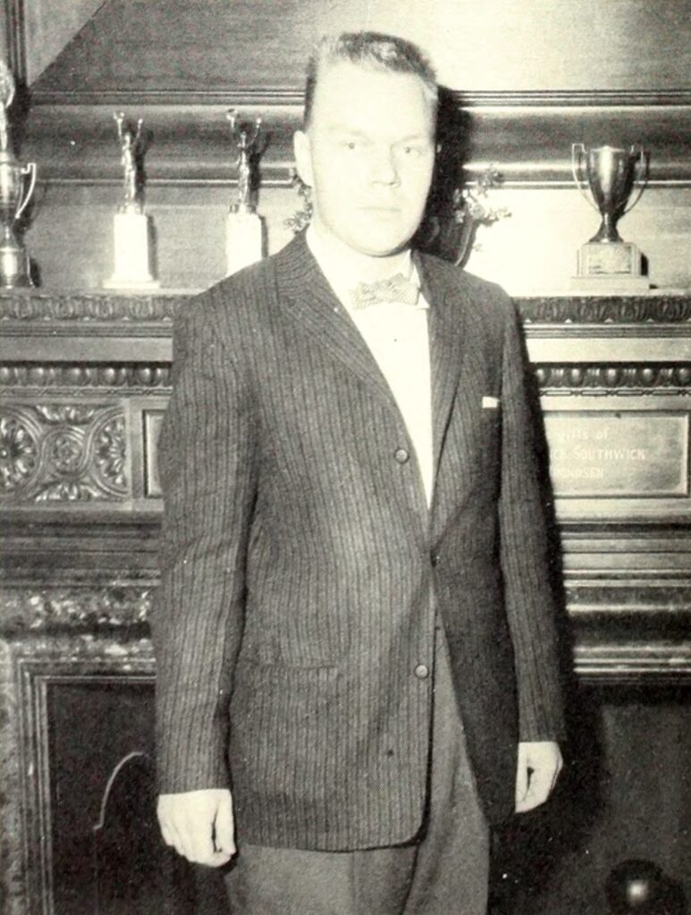 young man in suit in 1950s standing in front of fireplace