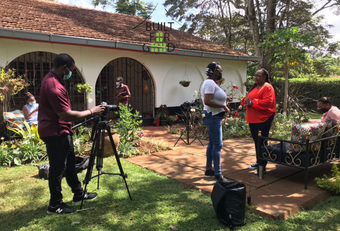 two woman talk as man adjusts camera on location outside a school in Kenya