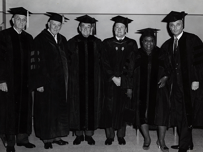 Norman Lear in cap and gown standing with other people in regalia