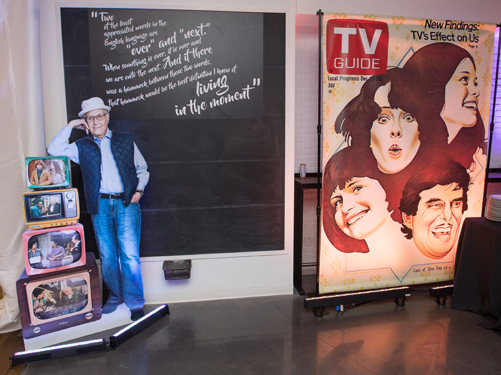 a life sized cutout, a blown up copy of TV Guide, and four TV consoles showing scenes from Lear's TV shows