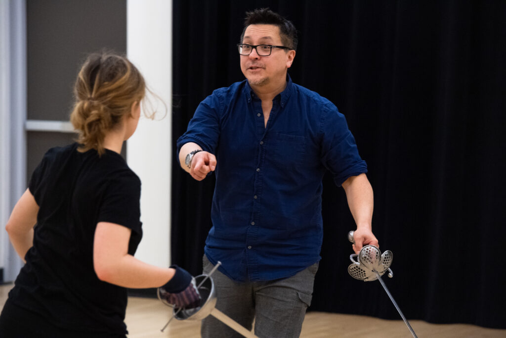 Ted Hewlett works with a student during a fight scene with swords