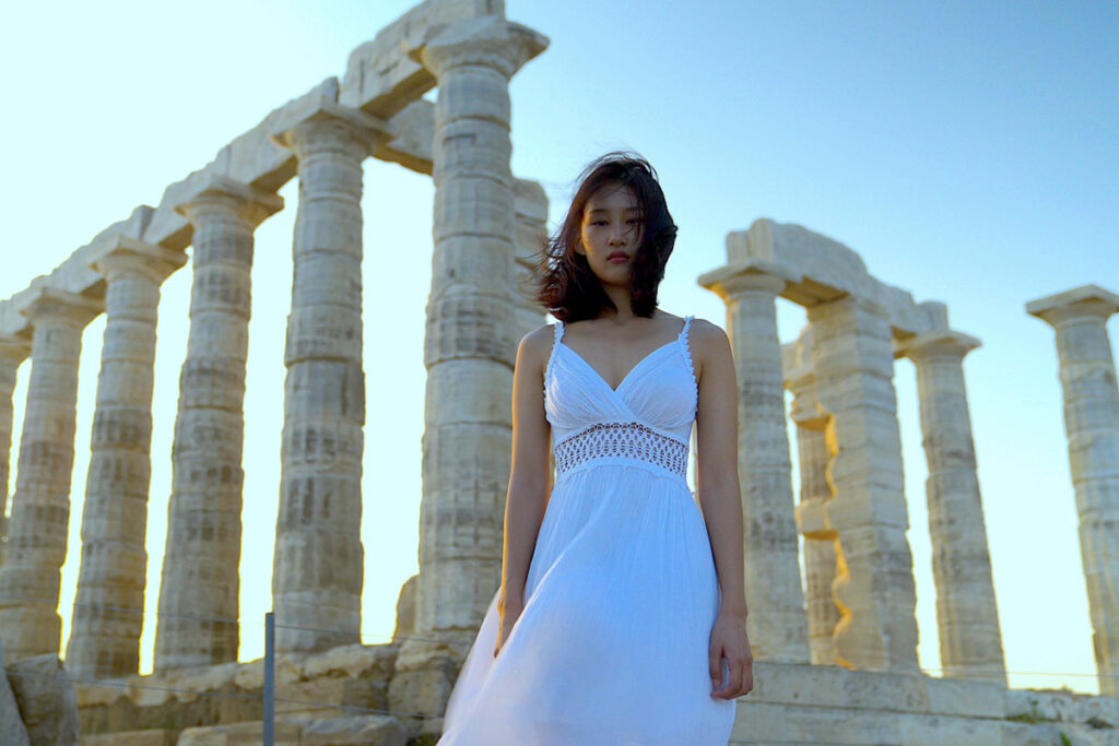 woman in white dress stands in front of Greek columns