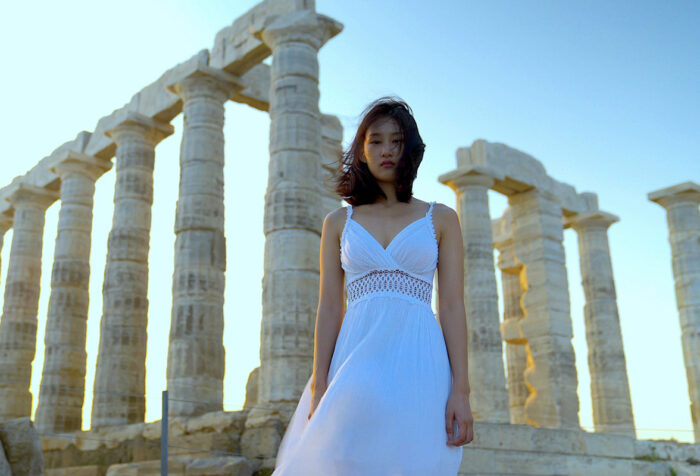woman in white dress stands in front of Greek columns