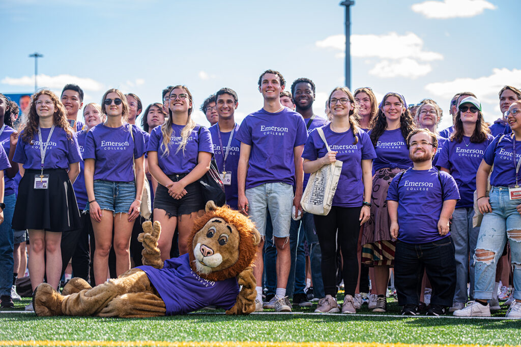Students in purple Ts stand for photo with Griff the Lion mascot lying on ground in front