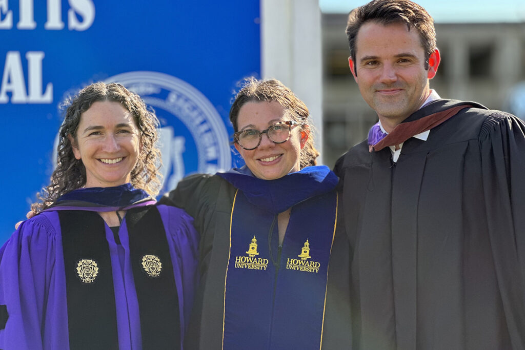 Two women and a man in academic regalia stand outdoors
