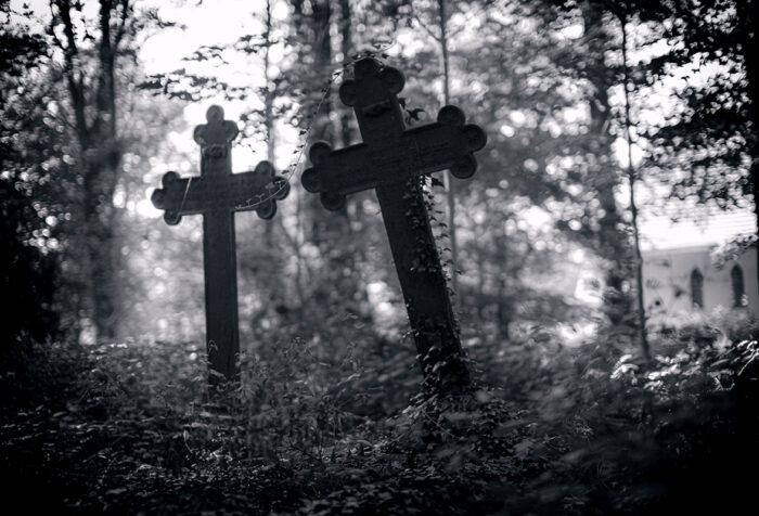 black and white photo of two cross-shaped graves in a wooded graveyard